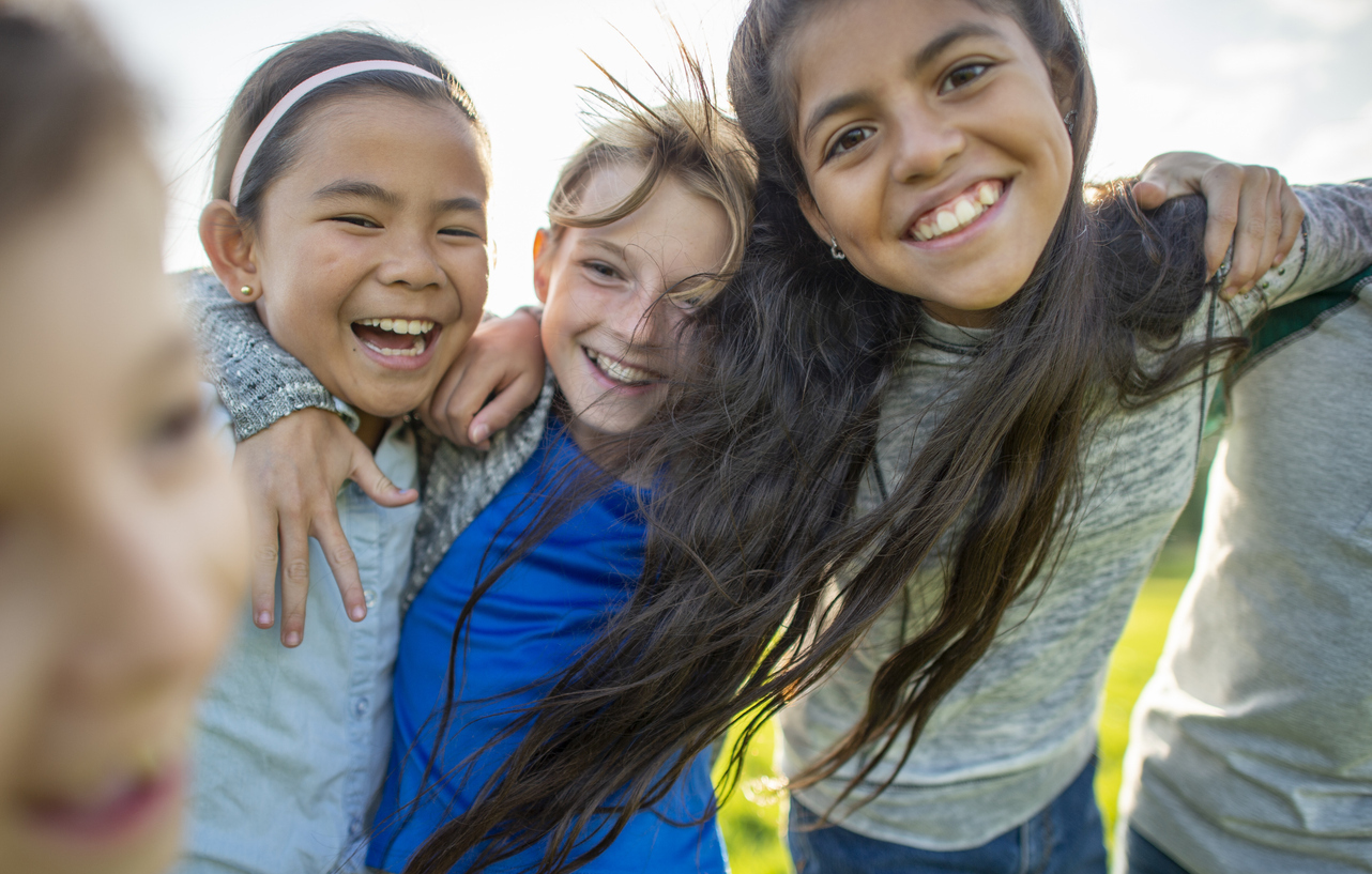 A small group of Elementary children huddle in closely to one another as they pose for a portrait.  They are each dressed casually and are smiling as they spend the time together.