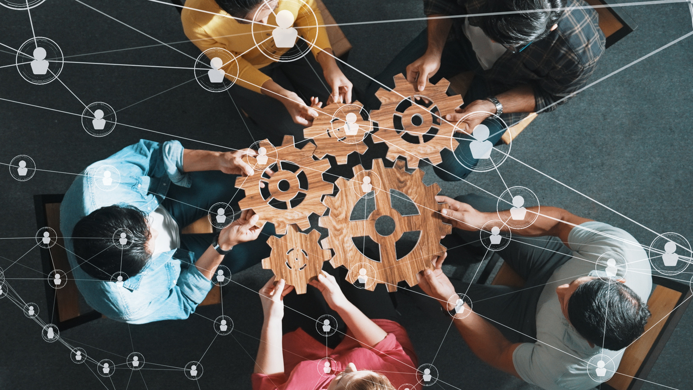 Top view of professional business people joining and gathering wooden gear together. Aerial view of diverse team working together to put or collect cog with network connection holographic. Symposium.