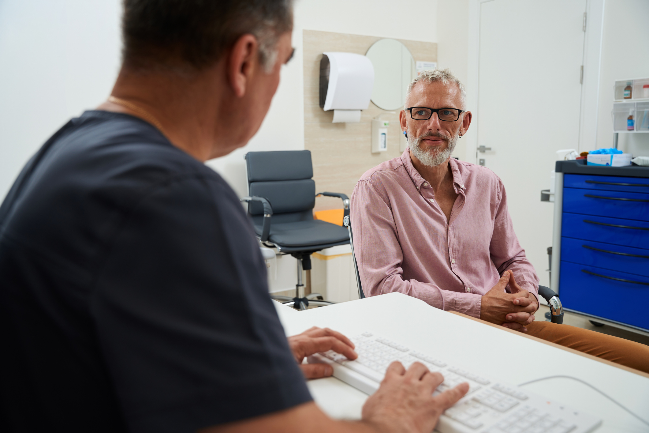 Bearded male with glasses at a doctors appointment, the men are seated at the office desk